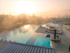 The sun's rays penetrate the fog over a swimming pool with slides