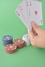 A hand presents four aces with assorted poker chips against a green backdrop