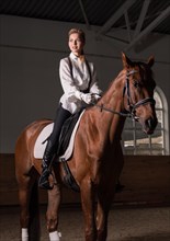 Image of a woman riding a thoroughbred horse. The background is a racing arena.
