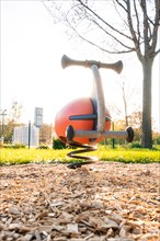 Orange spring rocker for children on a playground near a tree