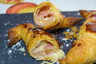 Croissant cut open revealing layers and ham and cheese filling with a shiny glaze