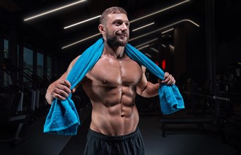 Muscular man posing in the gym with a towel on his shoulders. Fitness concept.