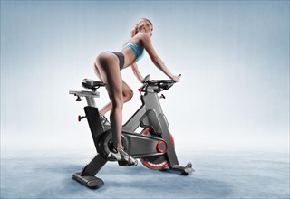 Beautiful slender and long-legged girl sits on an exercise bike. Side view. The concept of sports