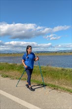 Outdoor enthusiast with walking poles beside a tranquil water body on a bright day