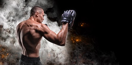 Muscular fighter posing with boxing paws against a background of smoke and fire. Mixed martial arts concept. High image quality