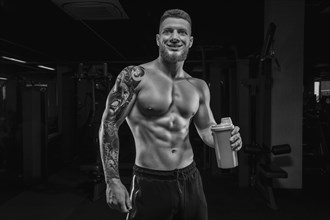Portrait of an athlete standing with a shaker in the gym. Bodybuilding and fitness concept.