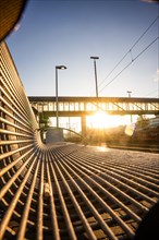 View along a metal grid of a bench onto an urban bridge architecture at sunset