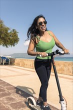 Young latina having fun with an electric scooter on the boardwalk