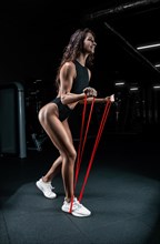 Tall athletic woman posing with gymnastic elastic bands in the gym. Fitness and bodybuilding concept.