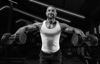 Handsome young man spreads his arms with dumbbells to the sides. Shoulder pumping. Fitness and bodybuilding concept.