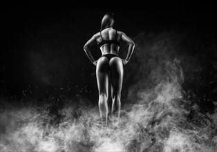 Image of a female athlete in a fire arena surrounded by smoke. Back view. Bodybuilding and fitness concept.