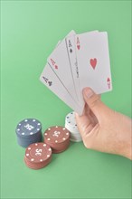A hand holding four aces above poker chips on a green background