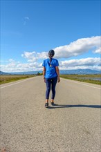 A traveler in casual attire treading along a paved road towards the horizon in a serene setting