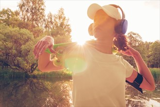 Image of a woman in a cap and headphones with a skateboard. Sunset in the park. Vacation concept.