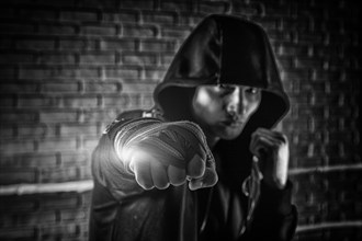 Boxer in a black sweatshirt and bandages wound on his hands beats his fist forward. The concept of sports
