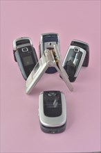 A collection of old cell phones with a flip phone in front on a pink background