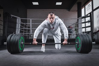 Athlete is standing on his knee and near the bar and is preparing to make a deadlift.