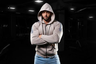 Muscular man poses in the gym in jeans and a sweatshirt. Sports