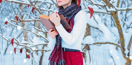 Portrait of a charming girl who reads a book in the winter forest. Concept of Christmas
