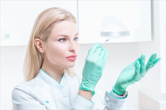 Portrait of a blonde girl in a medical gown with a syringe in her hands. Medical center advertisement.