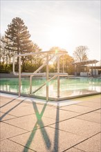 Light and shadow in an empty swimming pool with calm water and railings