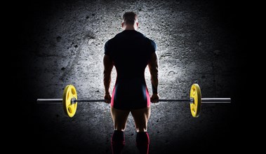 The athlete is standing with a barbell in his hands. Back view