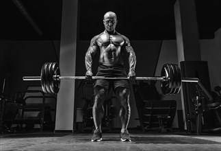 Muscular man stands with a barbell in his hands. Deadlift. Bodybuilding concept.
