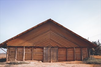 Front view of a wooden barn with a gable roof under a clear sky. Kampot