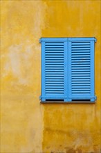 Blue shutter on yellow plaster wall