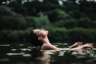 A young slender beautiful and hot girl with wet hair swims in the lake