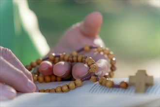 A woman's hands praying the rosary in the field over an open bible on a wooden table
