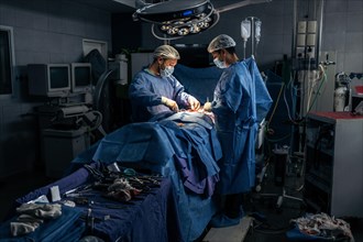 Wide view of a team of two surgeons operating on a patient in a dark OR at a hospital. Hospital surgery
