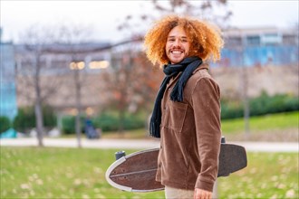 Portrait of an alternative man with skateboard smiling at camera standing on a park