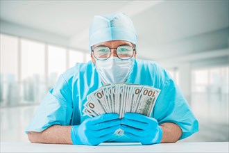 Portrait of a doctor holding hundred dollar bills. He is looking at the camera and smiling. The concept of corruption in medicine.