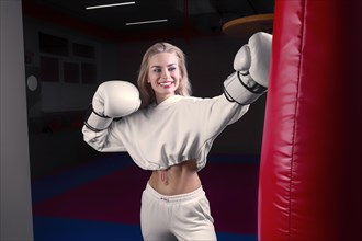 Cheerful and charming girl in a white sweatshirt boxing in huge gloves and smiling. The concept of sports