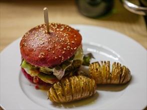 Delicious veggie burger in a beetroot bun with sliced potatoes