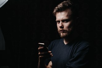 Handsome stylish bearded man holding a smartphone in his hands and looking at the camera