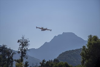 A fire-fighting aeroplane in flight in front of a mountainous landscape on a clear day