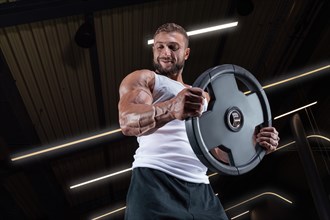 Portrait of a man in a white T-shirt exercising in the gym with barbell discs. Biceps pumping. Fitness and bodybuilding concept.
