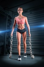 Sports girl trains in the gym against the background of the wall bars. She carries heavy metal chains in her hands. The concept of sports