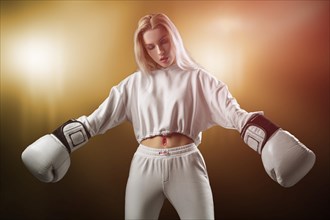 Charming girl in a white sweatshirt posing with huge white gloves. The concept of sports