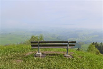 An empty bench stands in a meadow with a view of the mist-covered hills