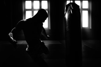 Athlete hits the bag. Dramatic light. The concept of kickboxing