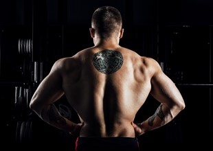 Huge weightlifter stands with his back to the camera and shows his huge back. Back view