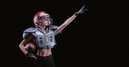 Image of a girl in the uniform of an American football team player. She points to an empty place. Black background. Sports concept. Shoulders pads.