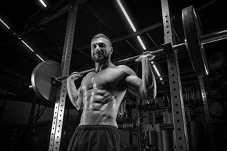Muscular man posing in the gym with a barbell. Fitness concept.