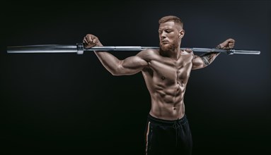 Young muscular guy posing with a barbell on his shoulders on a black background. Fitness and nutrition concept.