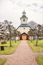Gravel path on a graveyard to an idyllic church in the Swedish countryside with pollarded trees