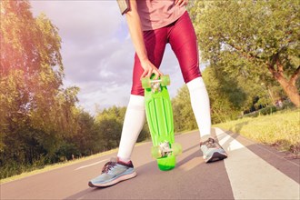 The girl holds a skateboard in her hands. Track in the park. Sports concept.