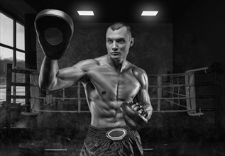 Brutal athlete holds boxing paws against the background of the ring. Mixed martial arts concept. High image quality